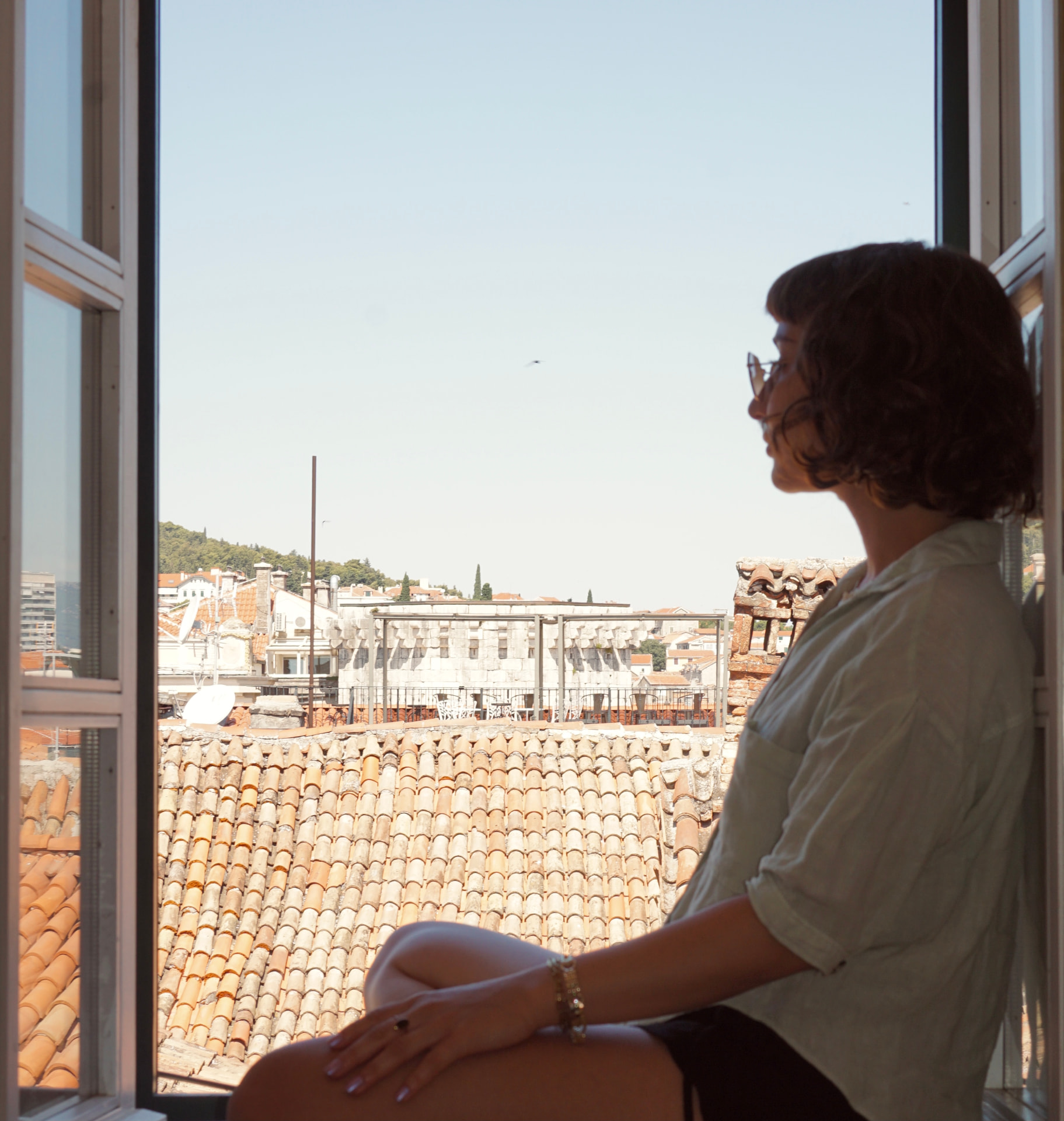 Stefanie Tezel am Fenster mit Blick über Dächer in der Nachmittagssonne