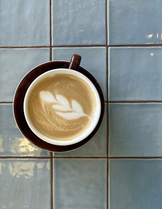 Cappuccino mit Latte-Art auf blauen Fliesen im Café Lou